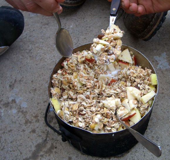 Железная кастрюля, стоящая на земле. Бирхер-мюсли едят вместе из одной посуды.