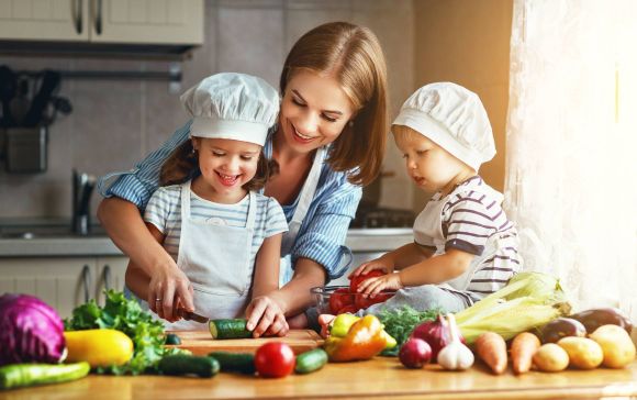 Mutter mit zwei Kleinkindern bereitet mit ihnen einen schmackhaften, veganen Gemüsesalat zu.