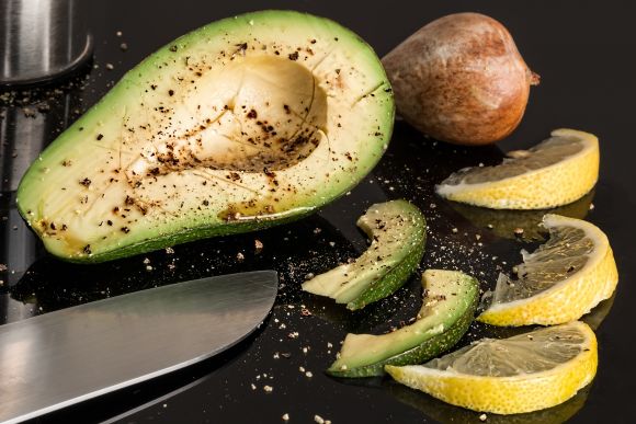 Avocado und Zitrone geschnitten auf schwarzer Fläche als Anfang eines frischen veganen Essens.
