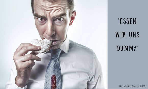 Ein Mann beisst mit gerunzelter Stirn in ein Junk-Food-Gebäck: Essen wir uns dumm?