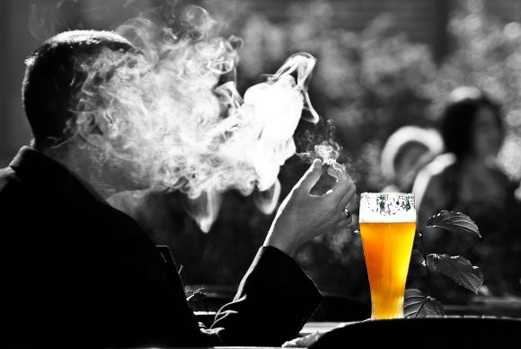 Man smoking in front of a glass of beer.