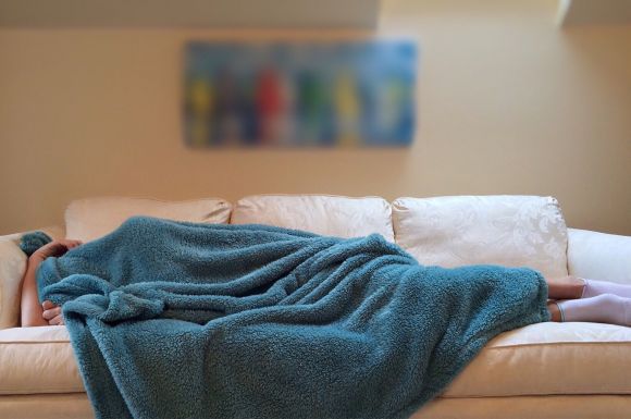 Person sleeping on a couch, fully covered with a blanket.