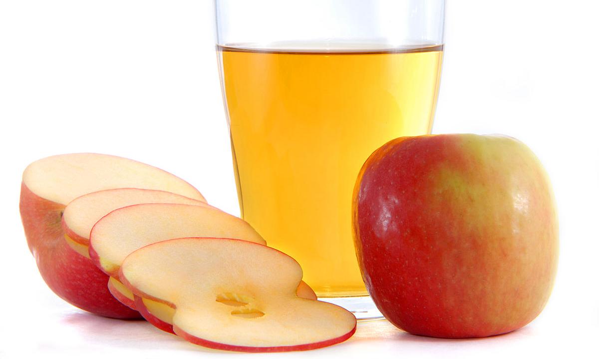Vaso lleno de vinagre de manzana, delante una manzana entera (derecha) y una cortada (izquierda). Vaso lleno de vinagre de manzana, delante una manzana entera (derecha) y una cortada (izquierda).