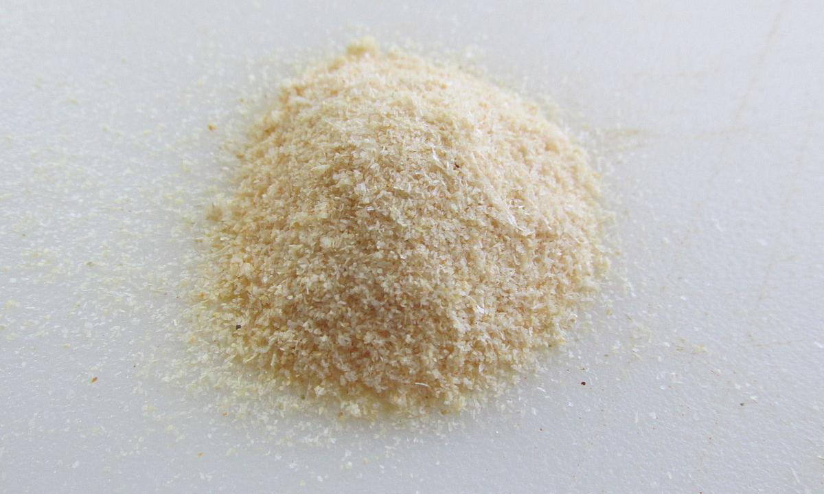 Granulated onion, in a heap on a light-gray table. (Allium cepa). Granulated onion, in a heap on a light-gray table. (Allium cepa).