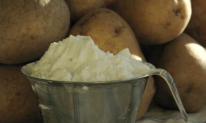 Vessel filled with potato flour, potatoes piled up in the background.