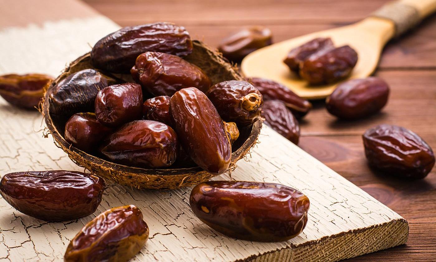 Кокосовая раковина на деревянной доске, заполненная датами, лежащая рядом с датами.