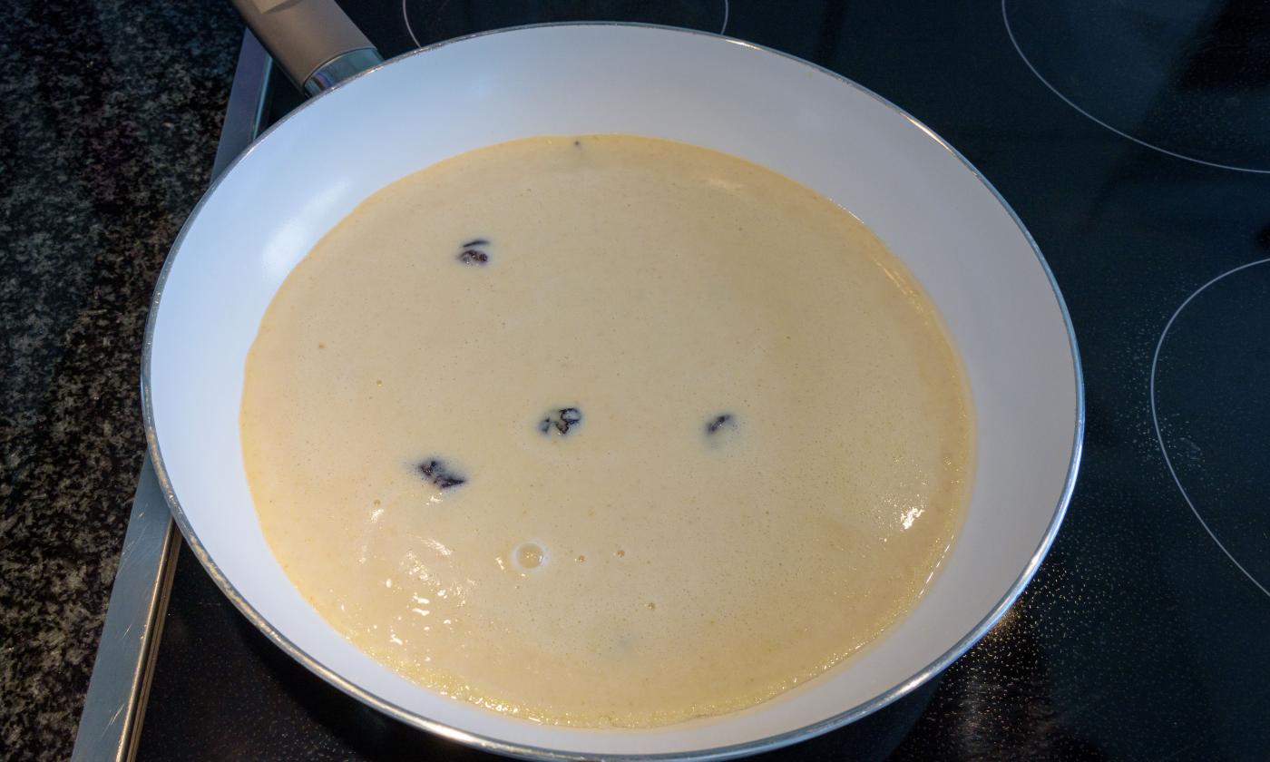 Masa batida lista para preparar «Tortitas austriacas Kaiserschmarrn con arándanos» en la sartén.