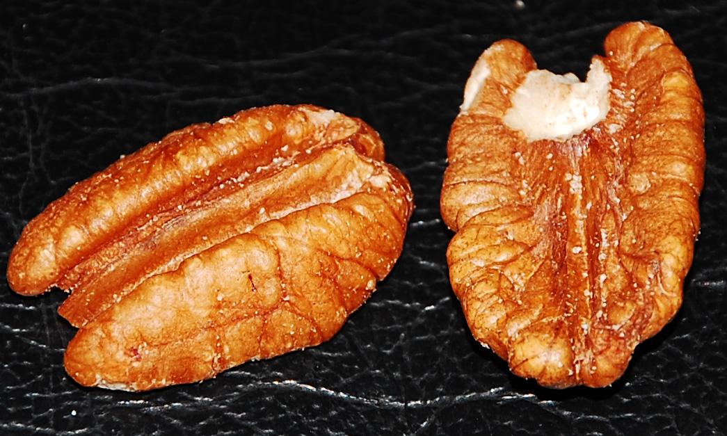 Primo piano di un pecan diviso in due, sgusciato (illinoinensis di Carya) su fondo nero.