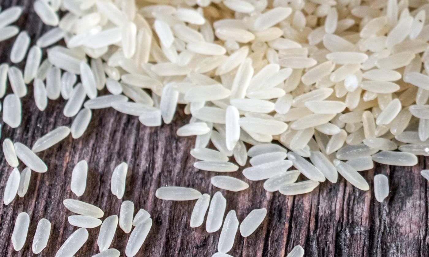 Langkornreis, weiss, roh - Oryza sativa L. - auf Holzoberfläche liegend.