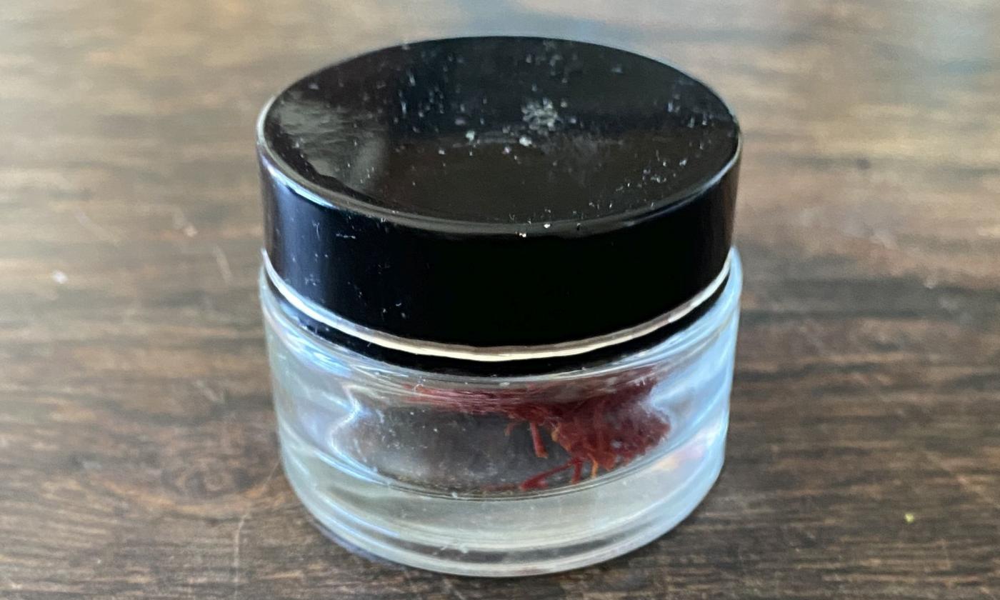 Safranfäden in kleiner neutraler Glasdose mit schwarzem Deckel auf sehr altem Holztisch. Safranfäden in kleiner neutraler Glasdose mit schwarzem Deckel auf sehr altem Holztisch.