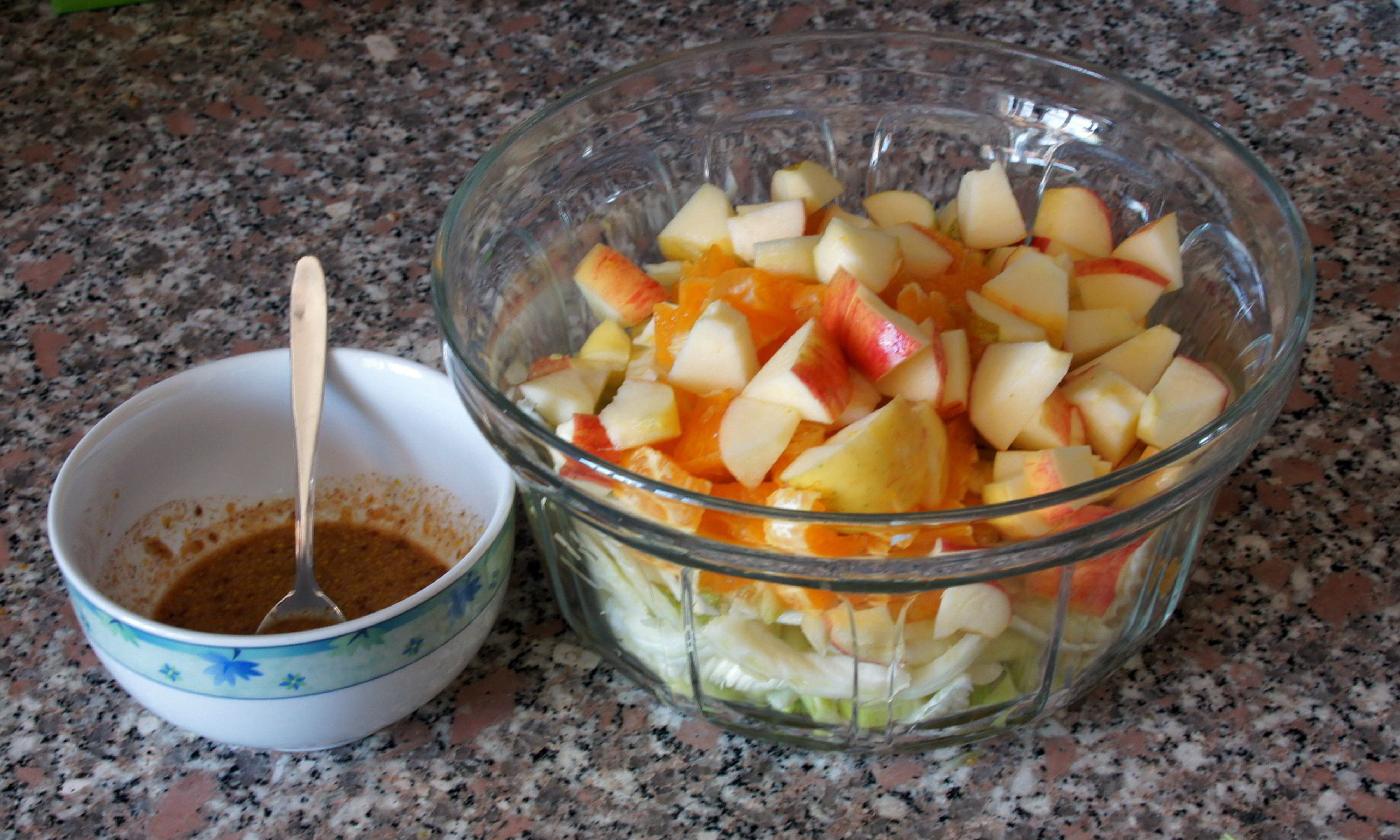 Все приготовленные ингредиенты для "Салата из фенхеля с яблоками и апельсинами" в стеклянной чашке и дрессингом в чашке слева.