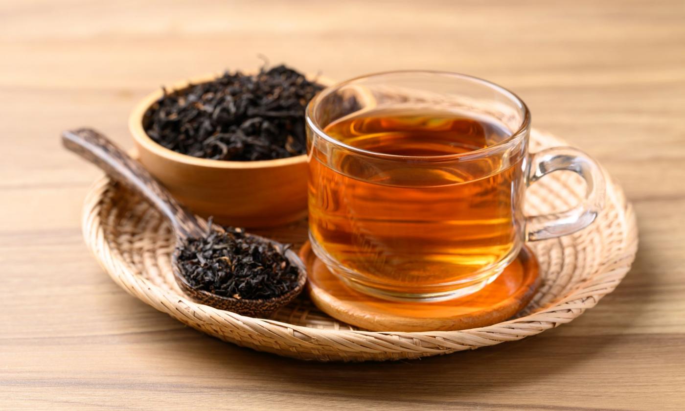 Schwarztee (Schwarzer Tee) in Glastasse. Daneben gewelkte, oxidierte und getrocknete Teeblätter. Schwarztee (Schwarzer Tee) in Glastasse. Daneben gewelkte, oxidierte und getrocknete Teeblätter.