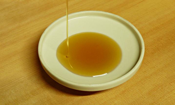 El aceite de sésamo de semillas tostadas gotea en un plato brillante sobre una superficie de madera. El aceite de sésamo de semillas tostadas gotea en un plato brillante sobre una superficie de madera.