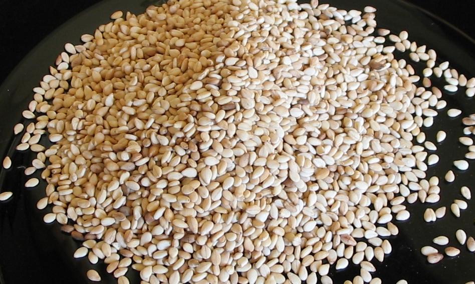 White  sesame seeds, heaped on a dark surface — seeds measure 2.5–3 mm long x 1.5 mm wide. White  sesame seeds, heaped on a dark surface — seeds measure 2.5–3 mm long x 1.5 mm wide.