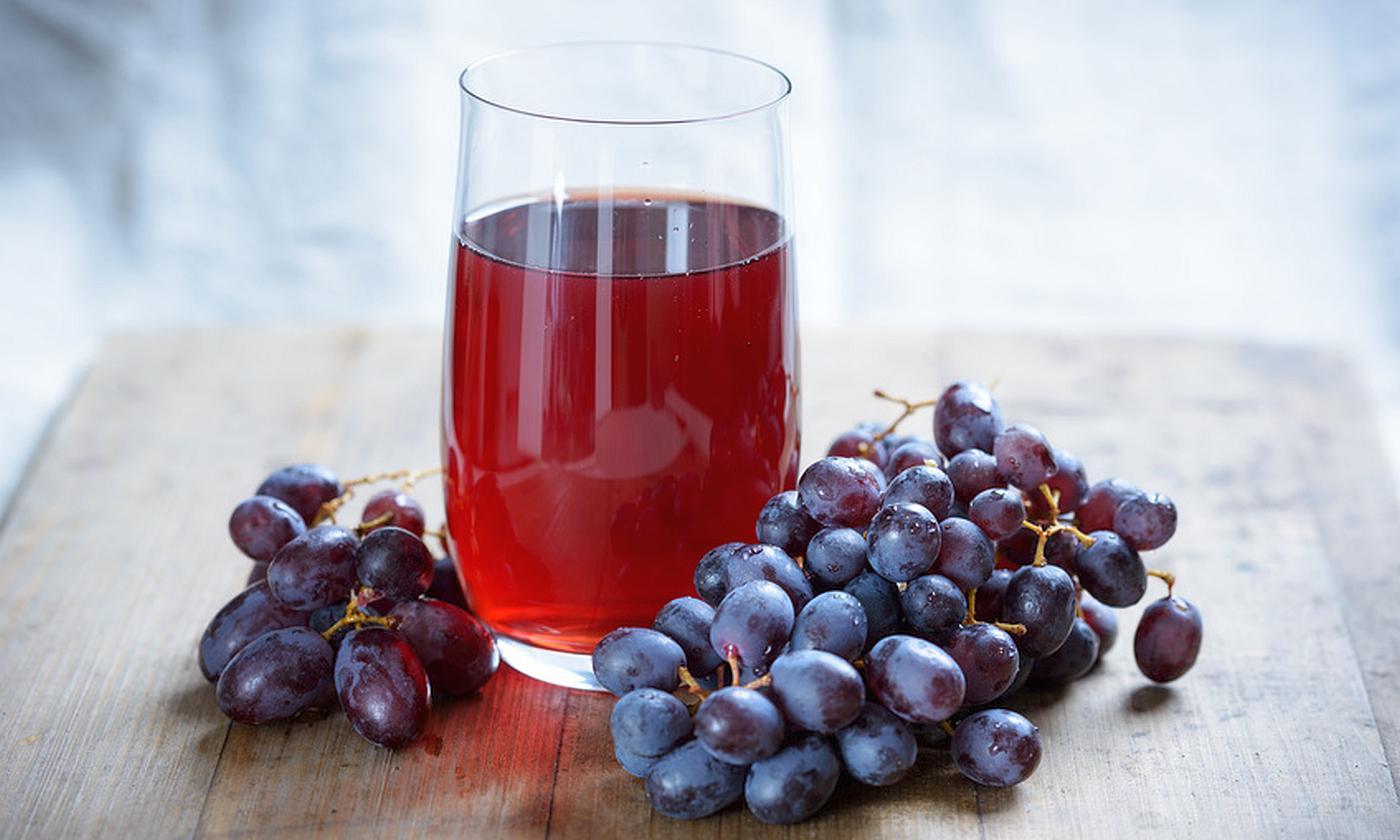 Zumo de uva roja en un vaso rodeado de uvas oscuras. Zumo de uva roja en un vaso rodeado de uvas oscuras.