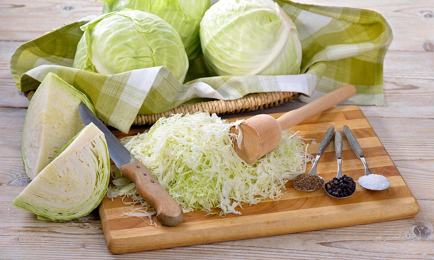 Weisskohl - auf Küchenbrett vorbereitet, um Sauerkraut herzustellen, dahinter Weisskohlköpfe. Weisskohl - auf Küchenbrett vorbereitet, um Sauerkraut herzustellen, dahinter Weisskohlköpfe.