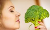 Junge Frau riecht an frischem Broccoli mit Strunk. Brassica oleracea var. italica
