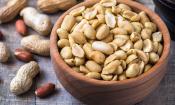 Erdnüsse ohne Schale und Haut in Holzgefäss, daneben Erdnüsse mit Schale oder bräunlich-roter Haut.