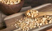 Cacahuetes tostados, pelados en tablero de mesa y cuchara de madera, detrás en un tazón de madera.