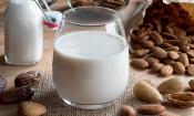 Leche de almendras en botella y vaso de agua rodeado de almendras con cáscara y almendras abiertas.