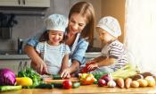 Mutter mit zwei Kleinkindern bereitet mit ihnen einen Gemüsesalat zu