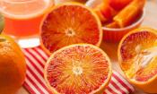 Orange, roh, mit Schale - Citrus sinensis: aufgeschnittene Früchte, dahinter Orangensaft.