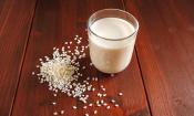Reismilch, nicht angereichert: Trinkglas mit Reismilch, daneben Reiskörner, verstreut auf Holz.