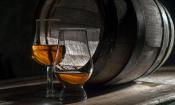 Destillierter Rum (40% vol) in zwei Gläsern vor traditionellem leeren, liegenden Holzfass.