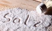 Salz bzw. Tafelsalz ausgestreut mit Salzstreuer auf Holztisch. Allgemein salzen wir viel zu viel.