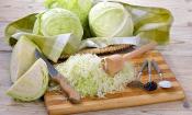 Weisskohl - auf Küchenbrett vorbereitet um Sauerkraut herzustellen, dahinter Weisskohlköpfe.