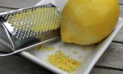 Zitrusreibe und angeriebene Zitrone mit Zitronenraspeln in eckiger Keramikschüssel.