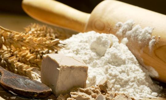 Brewer's yeast with flour and a rolling pin. Ears of wheat are in the background to the left, with a wooden spoon and fresh yeast cubes in the foreground. Brewer's yeast, here as traditional baker's yeast with flour and rolling pin. Left: wheat ears.