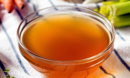 Organic vegetable broth (stock) with mushrooms, carrots and celery in glass bowl.