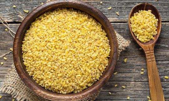 Cuenco de bulgur (trigo burgol) junto a una cuchara de madera.