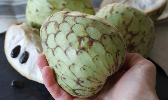 One hand holds a cherimoya (Annona cherimola), behind it also cut with kernels. One hand holds a cherimoya (Annona cherimola), behind it also cut with kernels.