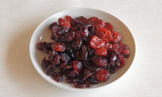 Getrocknete Cranberries in einer Schüssel: Getrocknete Cranberries haben einen herb-säuerlichen Geschmack. Sie dienen meist als Backzutat. Getrocknete Cranberries in weisser Schale. Moosbeeren haben einen herb-säuerlichen Geschmack.