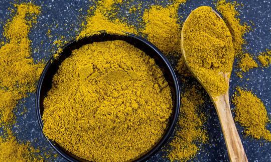 Curry in una ciotola nera e un cucchiaio di legno. Il curry è una miscela di circa 12 esp Curry in una ciotola nera e un cucchiaio di legno. Il curry è una miscela di circa 12 esp