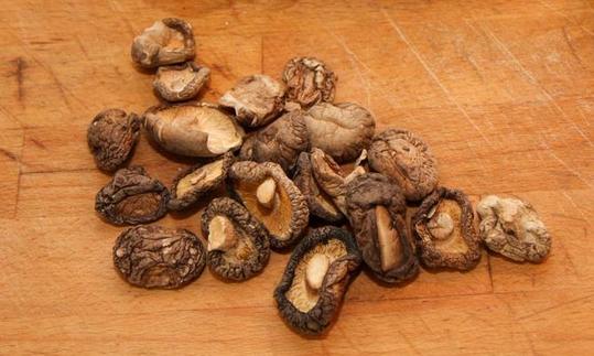 A number of dried shiitake mushrooms (Lentinula edodes) on a wooden cutting board A number of dried shiitake mushrooms (Lentinula edodes) on a wooden cutting board