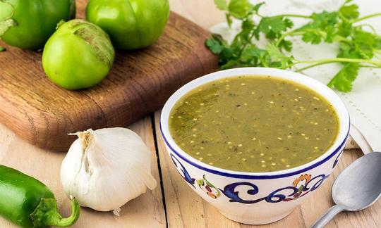 Salsa di peperone verde e tomatillos piccanti in una tazza, alcuni ingredienti accanto.