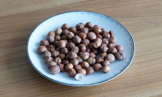 Las semillas de avellana son aptas para su consumo crudas, en ensaladas, como ingredientes para dulces, chocolate y mucho más. Nocciole crude e sbucciate su un piatto su un tavolo di legno.