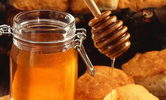 A jar containing honey and a honey dripper.