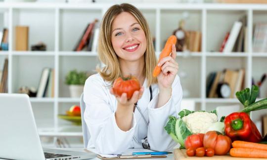 Портрет диетолога, показывающего свежие овощи в сыром виде.