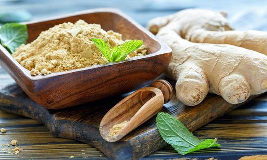 Ginger, raw - Zingiber officinale: A wooden bowl containing ground ginger is on the left. Ginger is usually purchased as fresh ginger root, shown on the right.