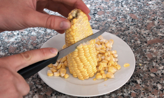 Для отделения кукурузных зёрен держите початок вертикально и ножом срезайте с него зёрна.
