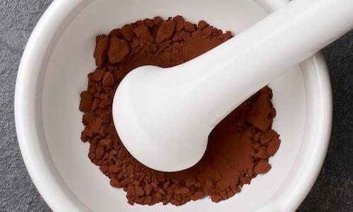Cacao in polvere, crudo, non zuccherato in un mortaio di ceramica bianca con pistillo.