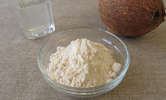Ciotola con farina di cocco. Cocos nucifera. Sullo sfondo a sinistra olio di cocco e a destra, un intero cocco.