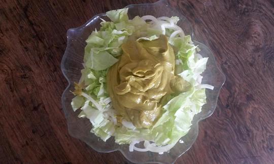 Vegan raw food avocado garlic cream as a salad dressing heaped on salad in glass bowl.