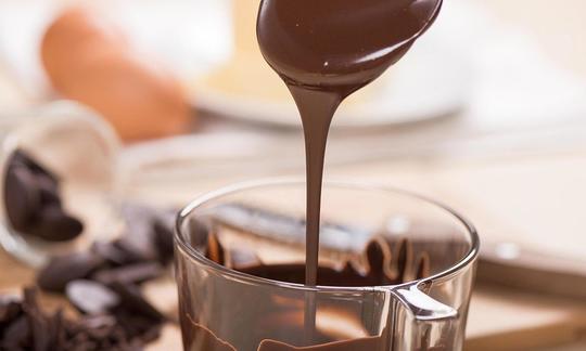 Dark couverture chocolate flowing from a spoon into a glass. Dark chocolate is the main ingredient. Dark couverture chocolate flowing from a spoon into a glass. Dark chocolate is the main ingredient.