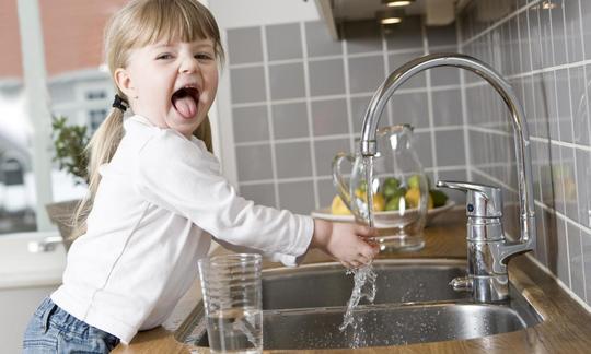Acqua del rubinetto (acqua potabile): ragazza che gioca con l'acqua potabile del rubinetto in cucina.