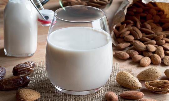 Almond milk in bottle and drinking glass surrounded by almonds with shell and open almonds.